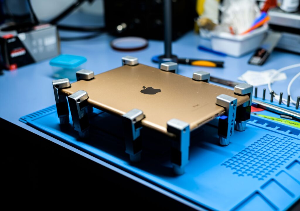 現在の画像: A close-up view of a tablet undergoing repair in a tech workshop with specialized tools.