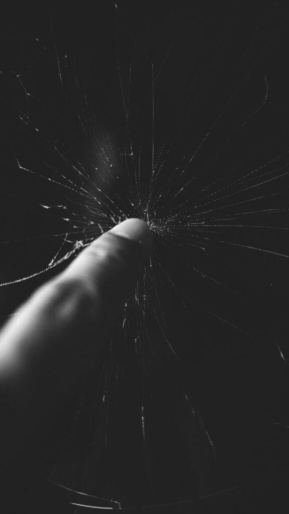 現在の画像: A dramatic black and white close-up of a finger touching cracked glass, emphasizing detail and texture.