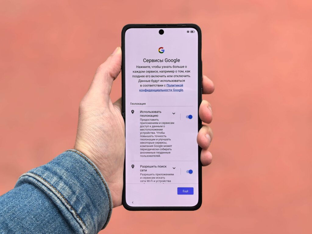 現在の画像: A person holding a smartphone displaying Google settings on a simple background.