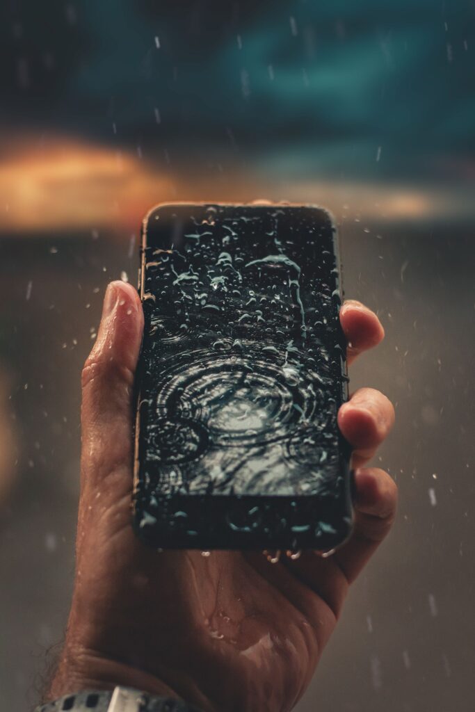 現在の画像: A person holds a smartphone with raindrops on screen, emphasizing water resistance.
