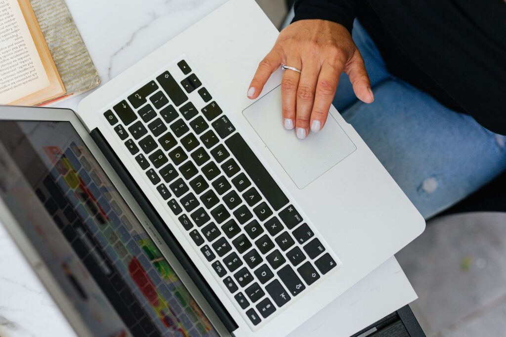 現在の画像: A person working on a laptop at a desk with an open book nearby, viewed from above.
