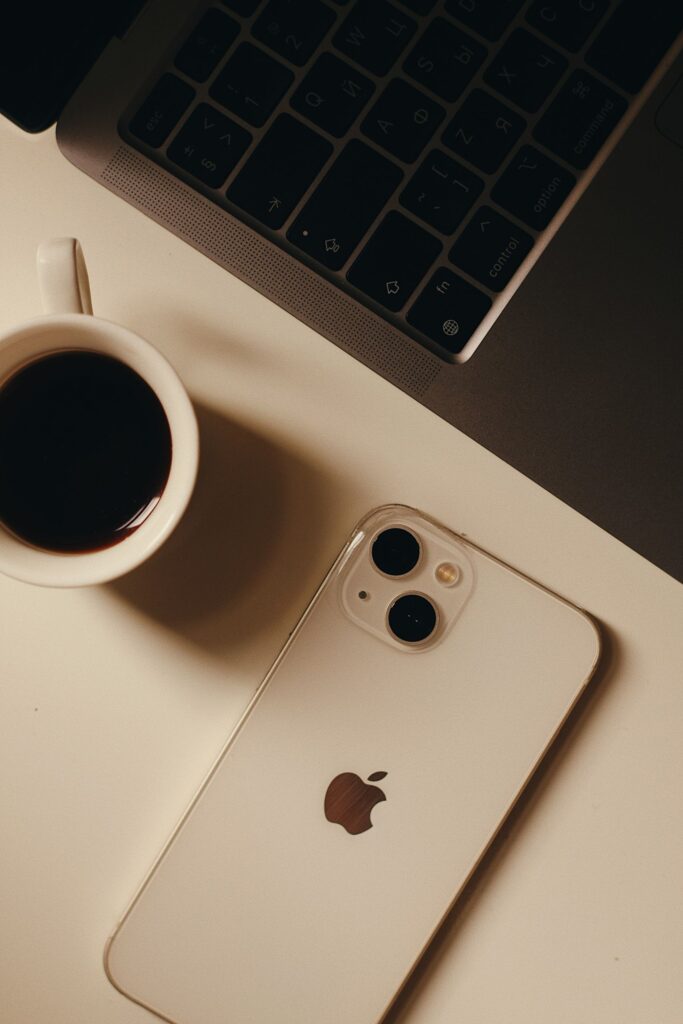現在の画像: A sleek setup featuring a cup of coffee, smartphone, and laptop on a desk.