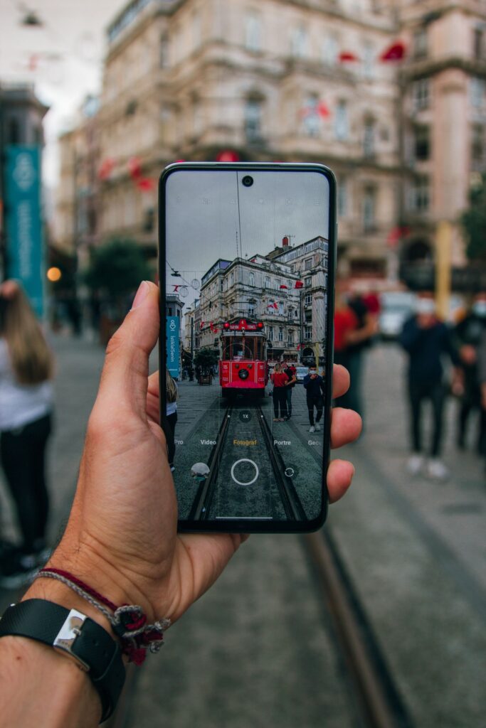 現在の画像: A vibrant street scene of a tram captured through a smartphone in an urban setting.