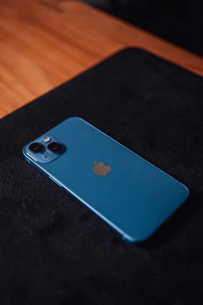 現在の画像: Blue smartphone on a dark surface with wooden table, emphasizing modern technology and design.