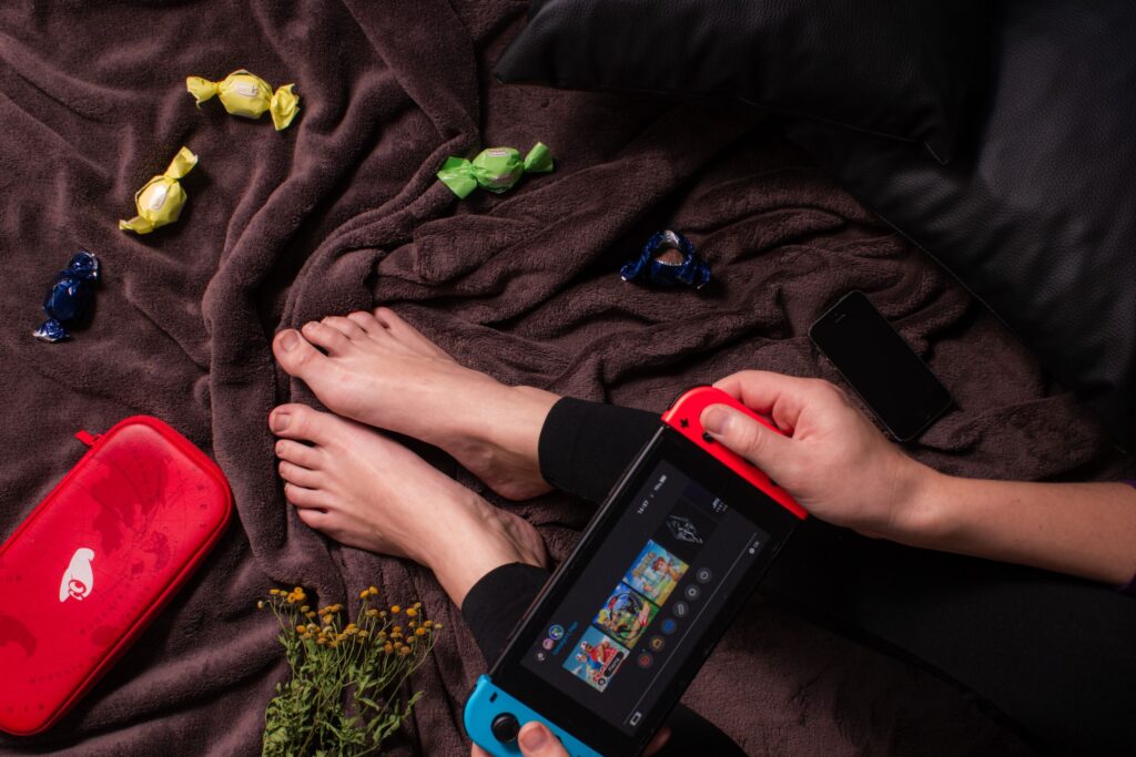現在の画像: Close-up of a person playing Nintendo Switch with candy and a cozy blanket.
