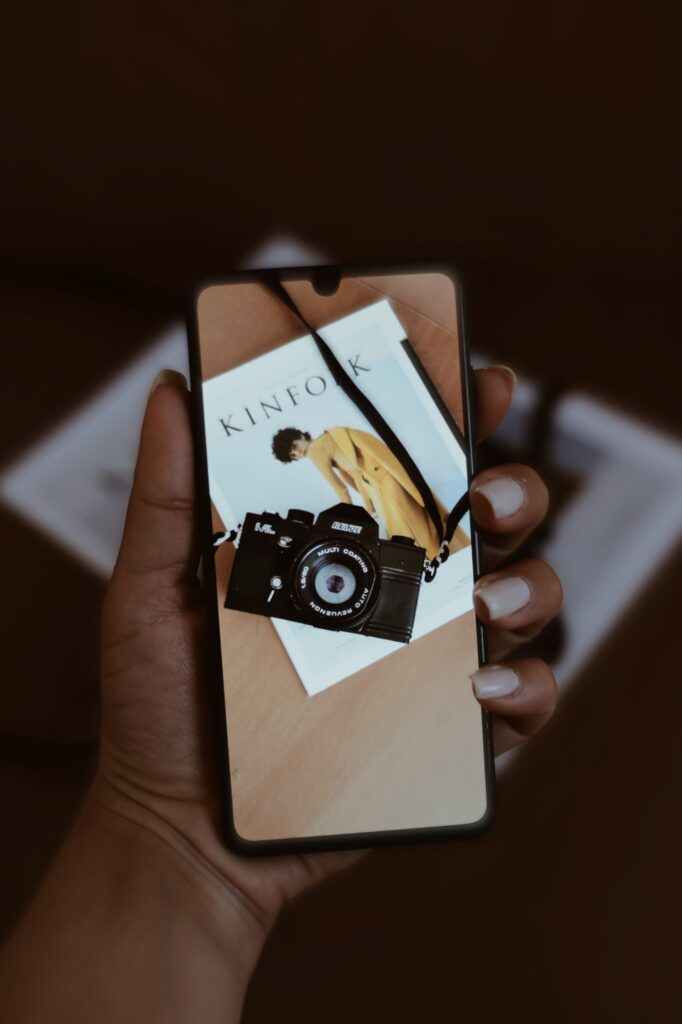 現在の画像: Hand displaying a smartphone showing a vintage camera, artistic and conceptual image.