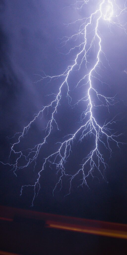 現在の画像: Intense lightning bolt illuminating a dark night sky during a powerful thunderstorm.