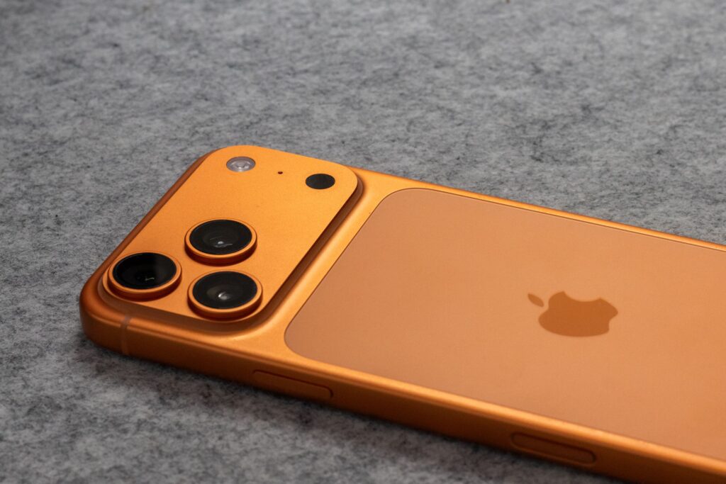現在の画像: Orange smartphone with dual cameras placed on a soft gray fabric surface.