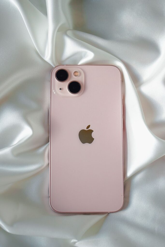 現在の画像: Pink smartphone with dual cameras placed on luxurious white satin fabric.