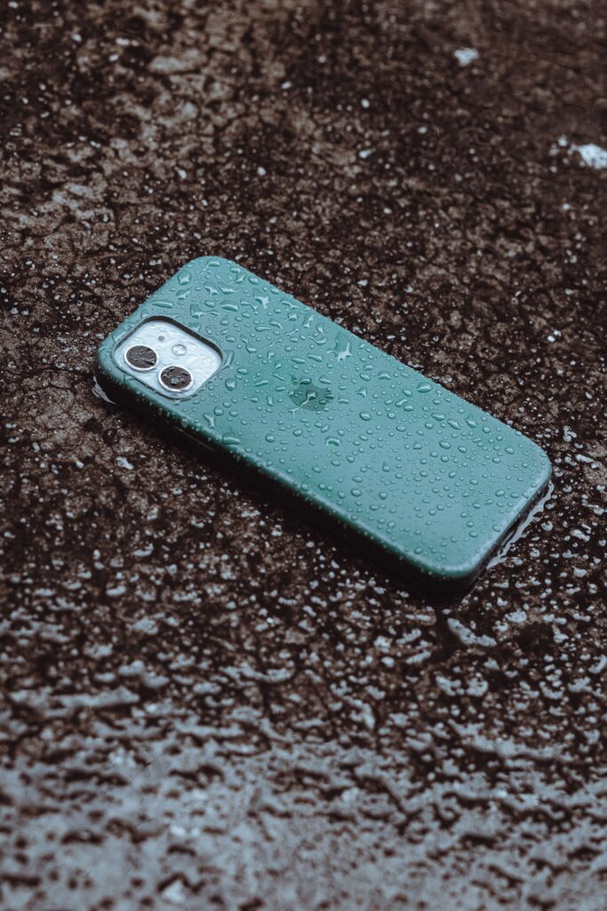 現在の画像: Rain-soaked smartphone lying on wet pavement, showcasing waterproof design.