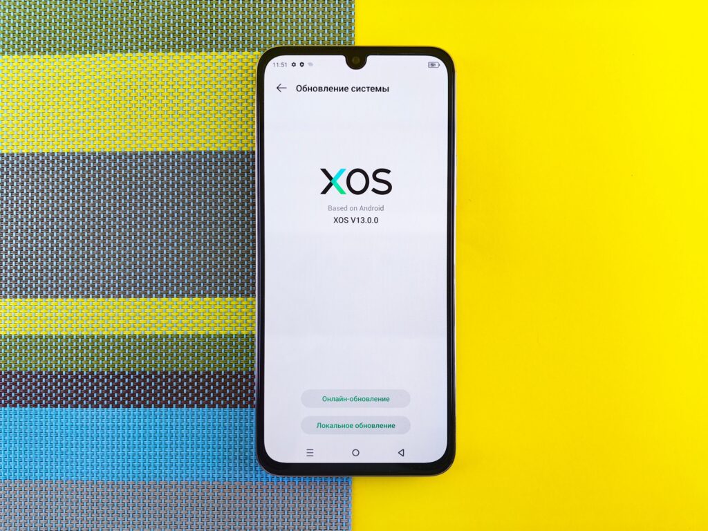 現在の画像: Smartphone on colorful background showing XOS version update, based on Android.