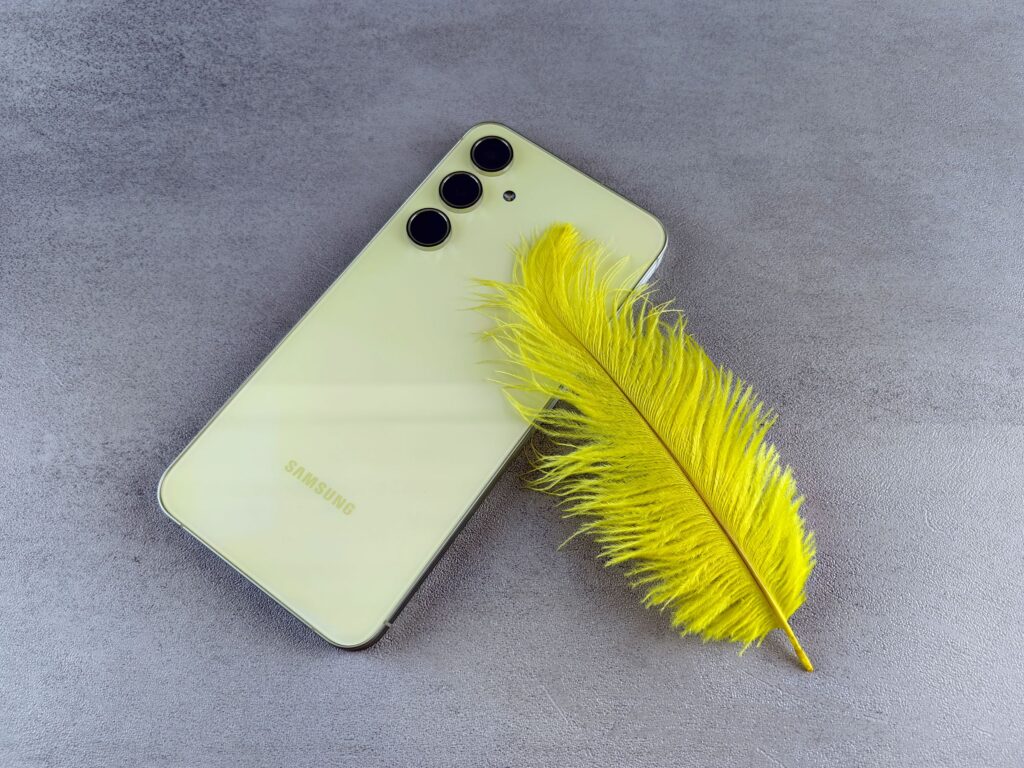 現在の画像: Stylish yellow feather next to a sleek smartphone, capturing elegance and technology together on a gray surface.